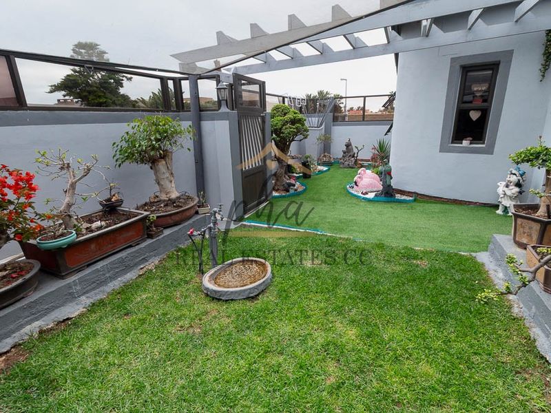 A well-maintained rear garden area featuring a pergola, boundary wall, gate, and a combination of natural and artificial lawn surfaces.
