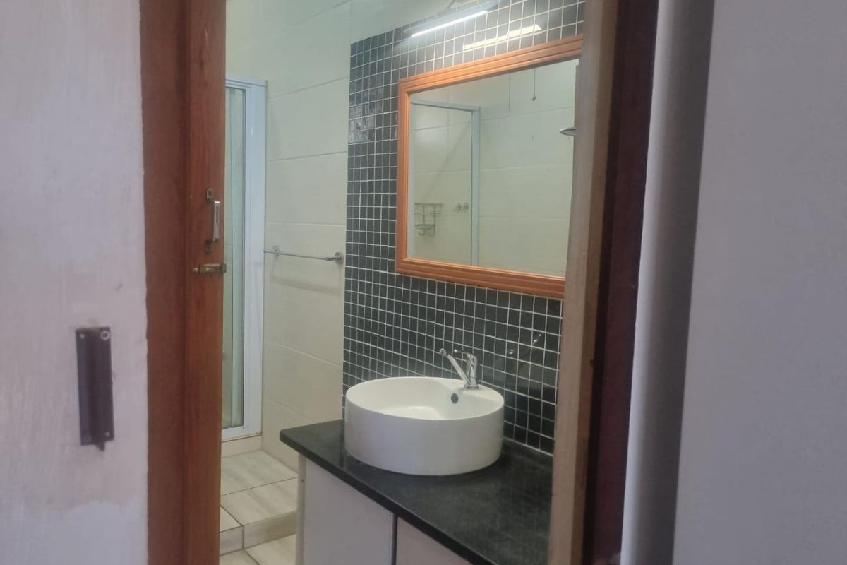 A clean bathroom featuring a modern vessel sink on a granite vanity, tiled splashback, wall mirror, and a separate shower enclosure.