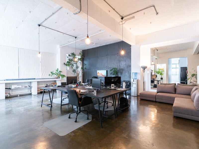 Modern open-plan office space featuring polished concrete floors, exposed industrial ceilings with conduit, and a striking dark feature wall.