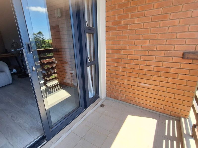 A private balcony featuring a tiled floor, exposed brick wall, and timber balustrade, accessible via a large sliding glass door.