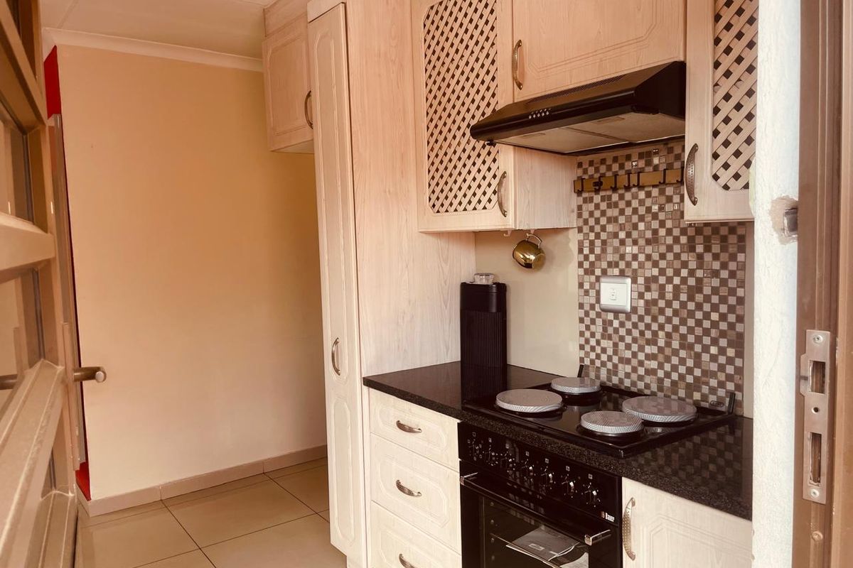 Compact kitchen featuring light wood-finish cabinetry, dark granite countertops, a built-in oven with electric hob, and a decorative tiled splashback.