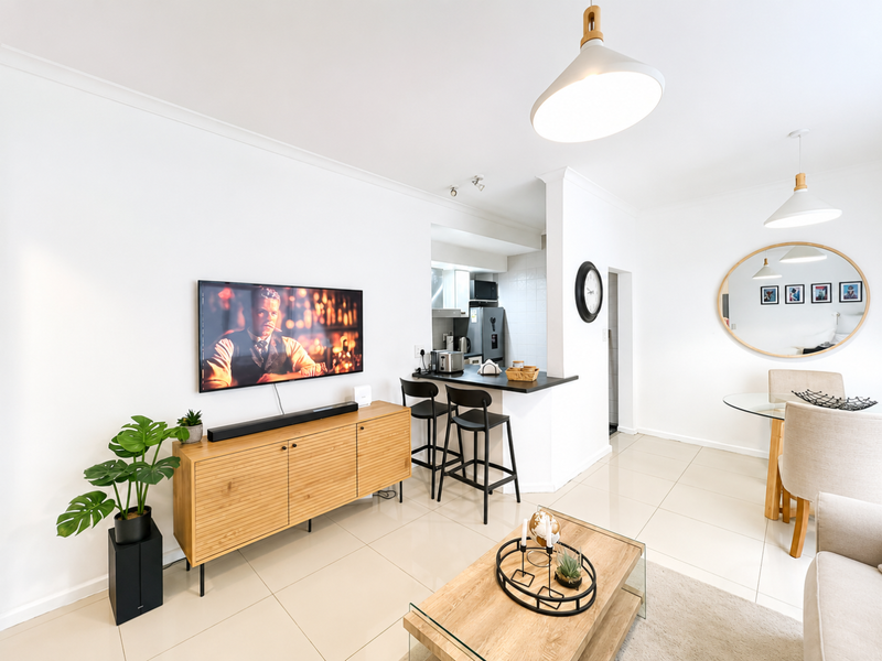 Bright open-plan living and dining area featuring large format floor tiles, a breakfast bar, and modern pendant lighting, creating a cohesive and functional space.