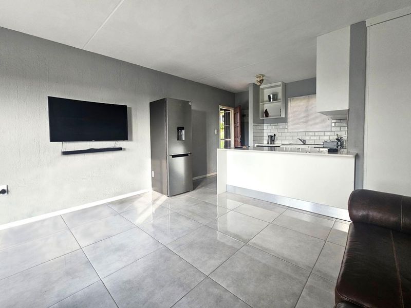 Open-plan living area featuring a modern kitchen with subway tile backsplash, a central island, and neutral ceramic floor tiles throughout.