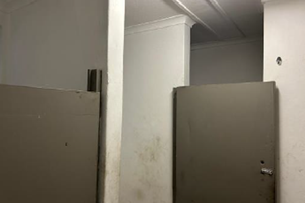 A utilitarian restroom area featuring partitioned stalls with worn surfaces and visible wall damage, requiring maintenance and cosmetic updates.