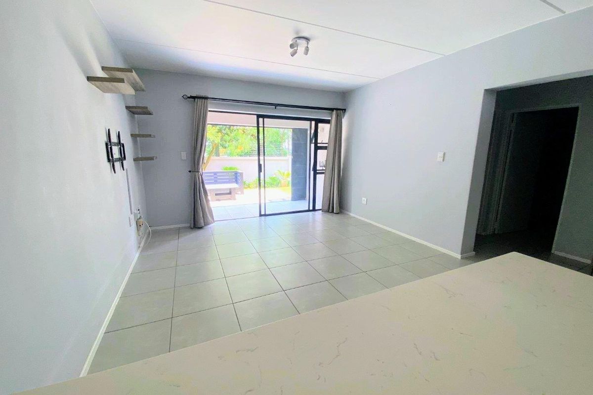 Bright open-plan living area featuring neutral tiled flooring, floating shelves, and a sliding glass door providing direct access to the outdoor patio space.