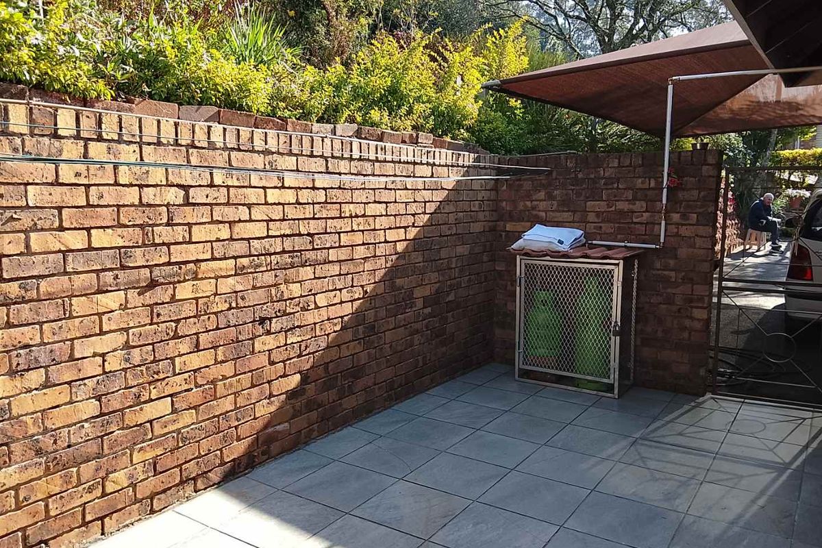 A paved rear courtyard area featuring a brick boundary wall, a retractable awning, and a secure gas bottle storage cage.