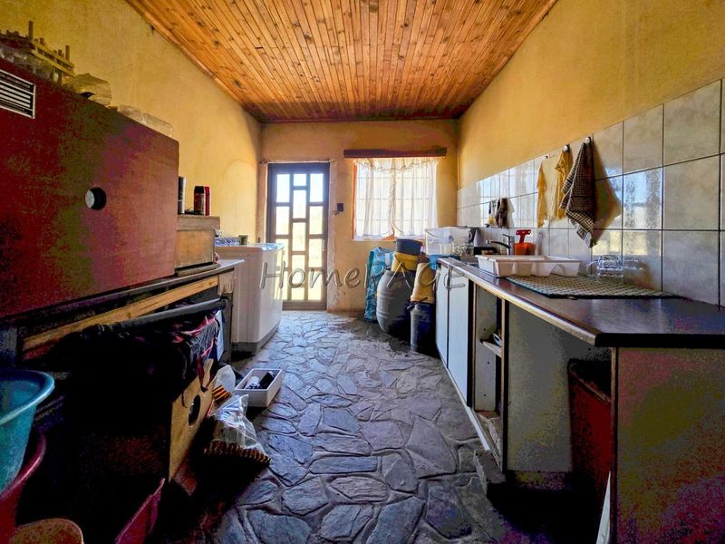 A functional scullery area featuring stone flooring, timber ceiling, and built-in cabinetry with a sink, requiring cosmetic updates to modernize the space.