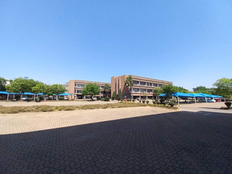 Exterior view of a multi-story brick office building featuring paved parking areas and blue shade-cloth carports.