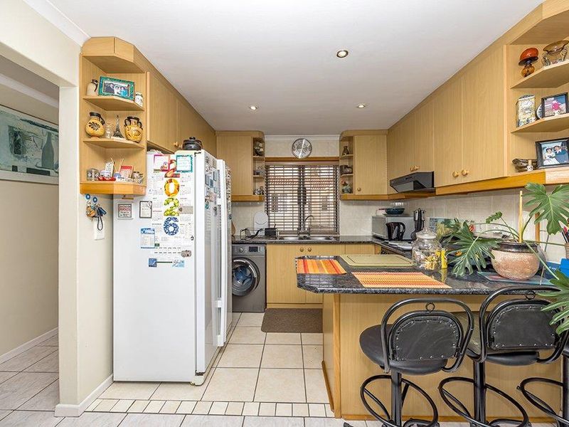 Functional kitchen featuring light wood-tone cabinetry, granite countertops, a breakfast bar, and tiled flooring with integrated laundry appliance space.