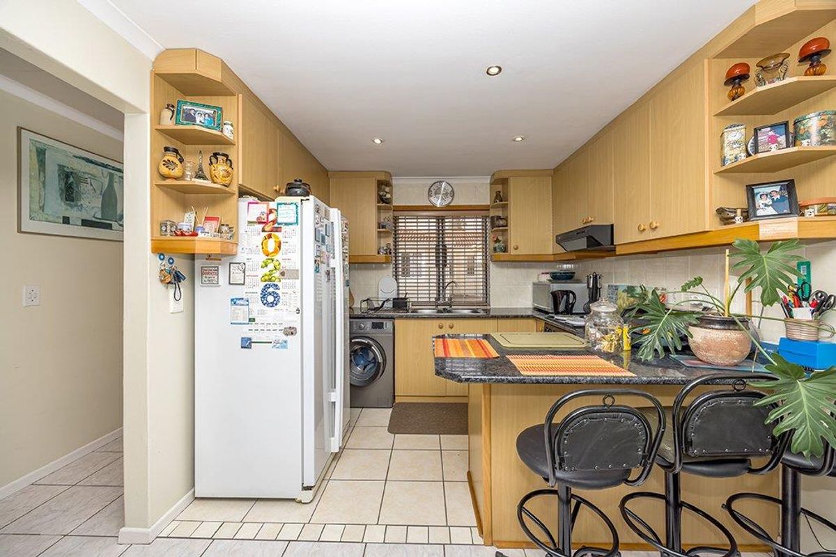 Functional kitchen featuring light wood-tone cabinetry, granite countertops, a breakfast bar, and tiled flooring with integrated laundry appliance space.