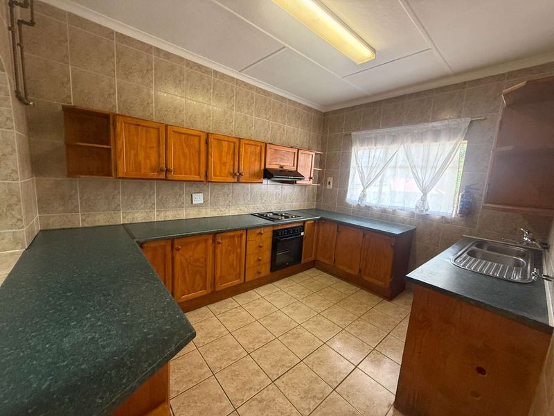 A functional kitchen featuring wooden cabinetry, laminate countertops, a built-in oven with gas hob, and tiled finishes throughout.
