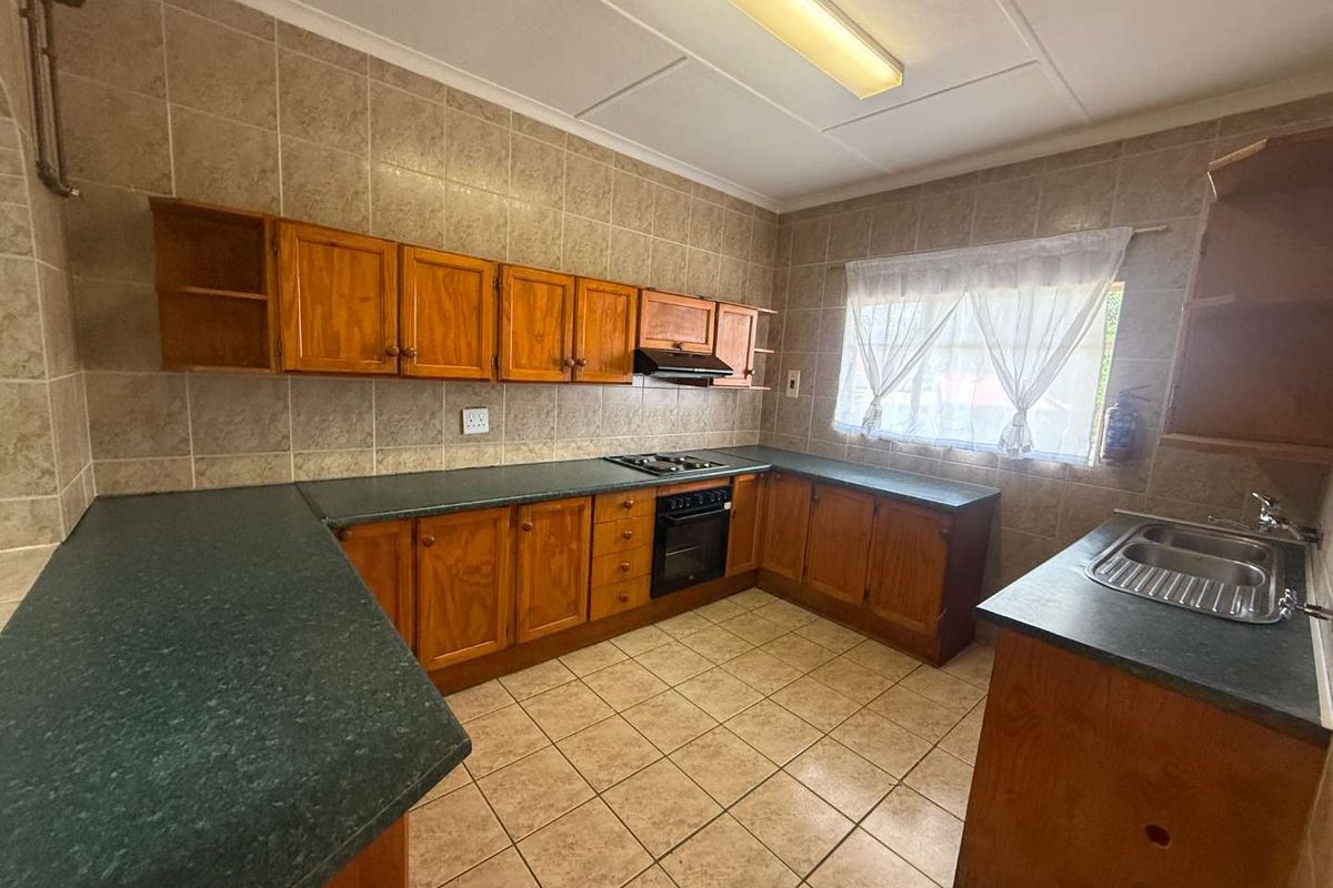A functional kitchen featuring wooden cabinetry, laminate countertops, a built-in oven with gas hob, and tiled finishes throughout.