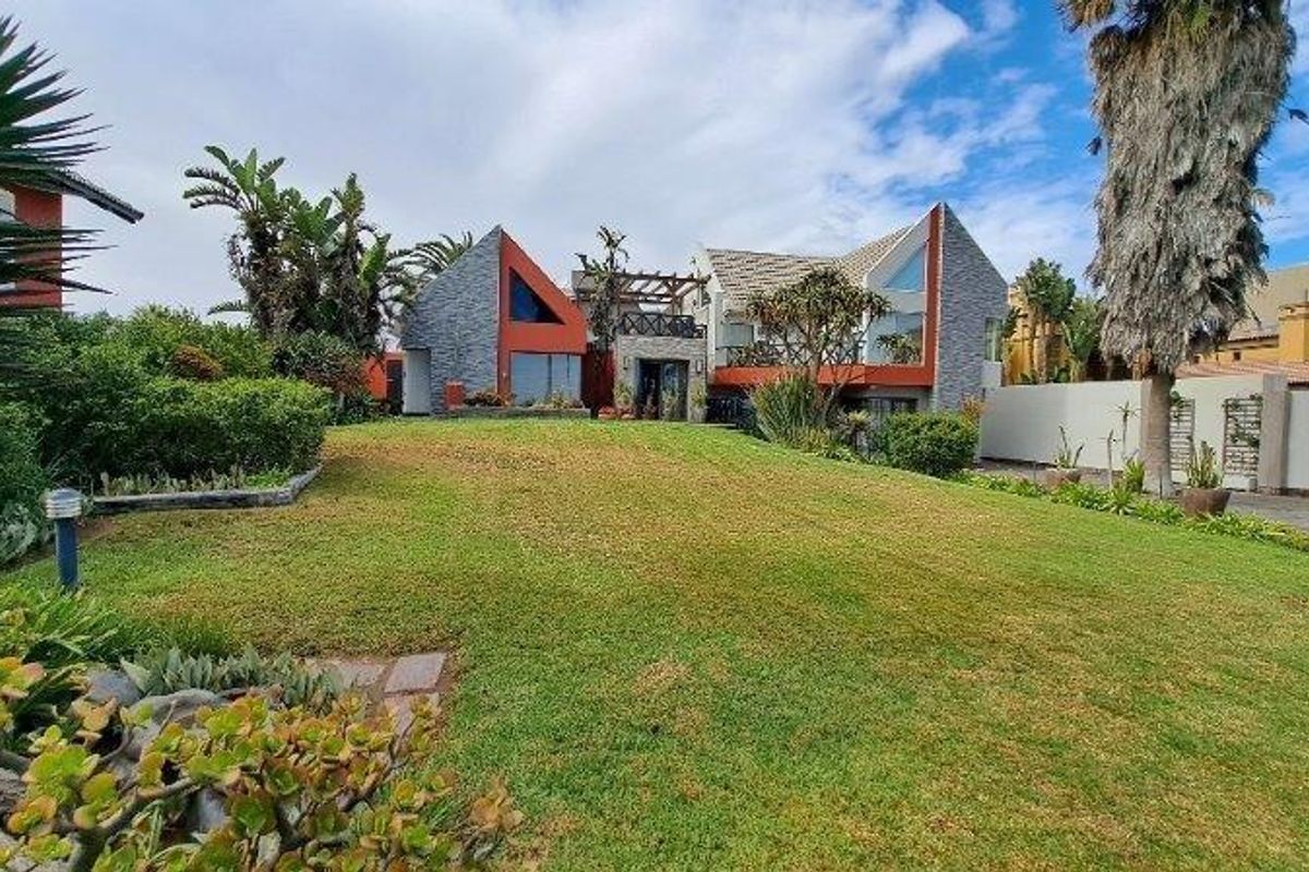 A spacious rear garden featuring a well-maintained lawn, established landscaping, and a view of the multi-level residential property with unique architectural design.