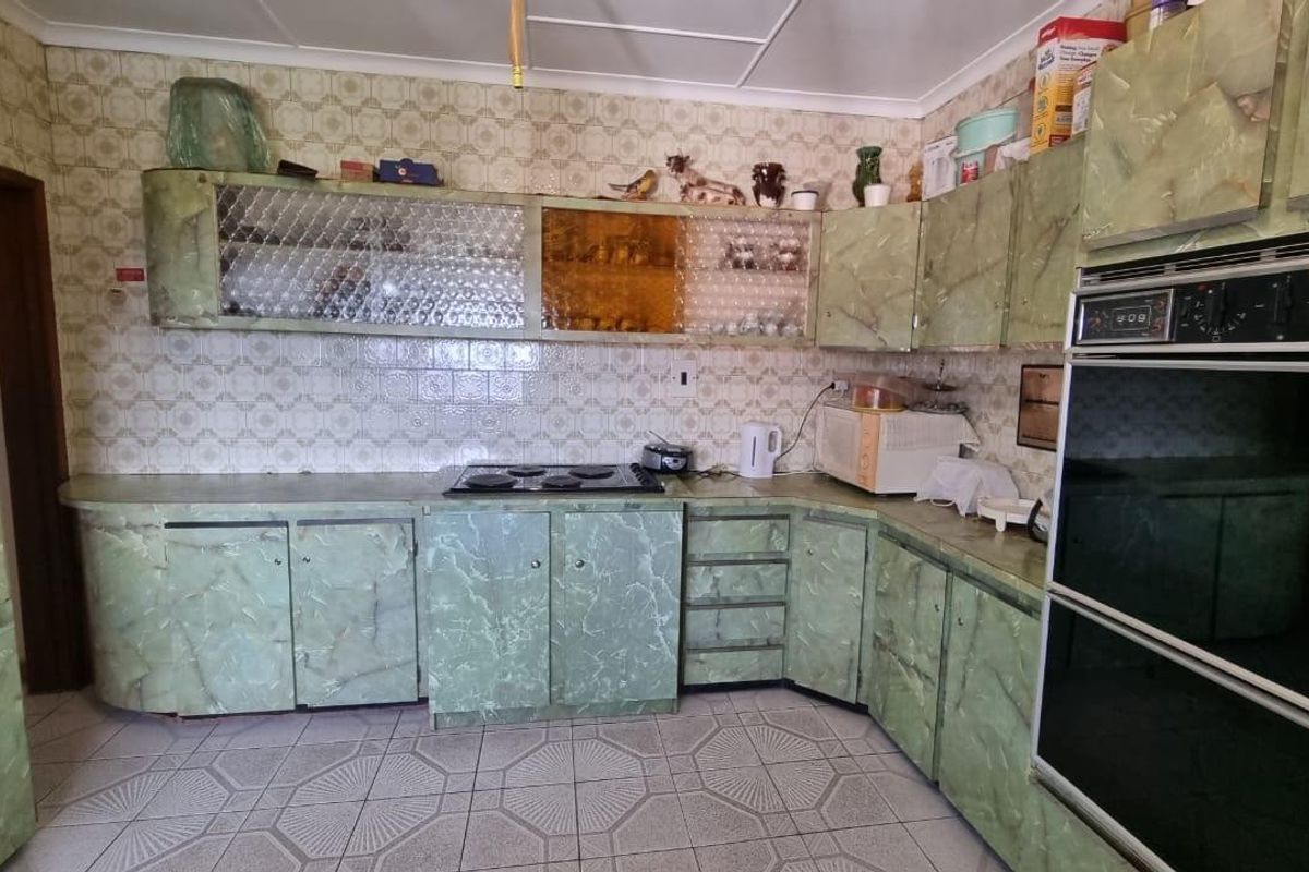 A dated kitchen featuring original green marble-effect cabinetry, integrated oven, electric hob, and patterned wall tiles, offering significant potential for a modern renovation.