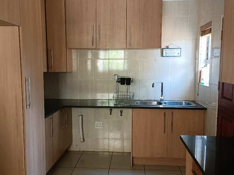 A functional kitchen featuring laminate cabinetry, granite countertops, a double bowl sink, and tiled backsplash with neutral ceramic floor tiles.