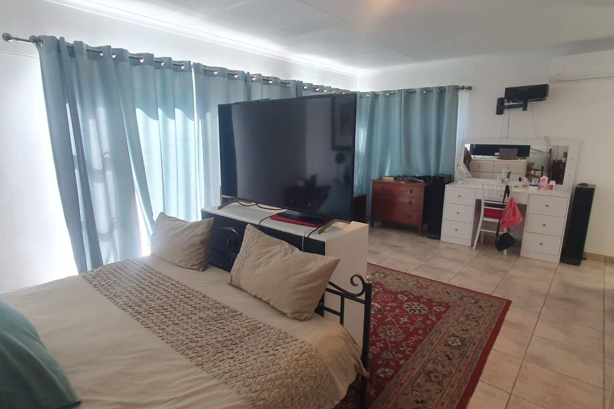Spacious bedroom featuring tiled flooring, large windows with curtain tracks, and a wall-mounted television bracket.