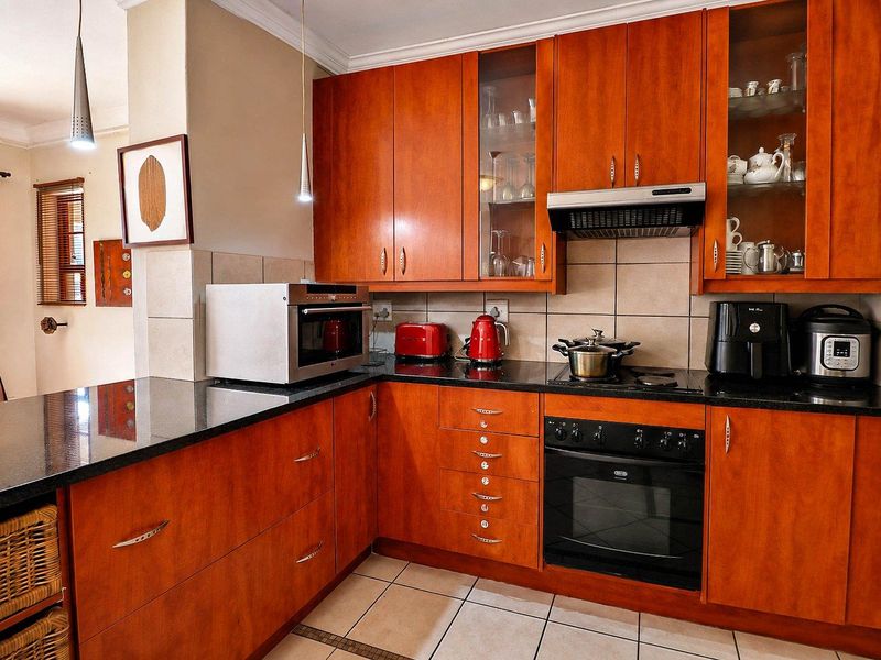 A functional kitchen featuring warm-toned wooden cabinetry, black granite countertops, built-in oven, electric cooktop, and tiled flooring with a neutral backsplash.