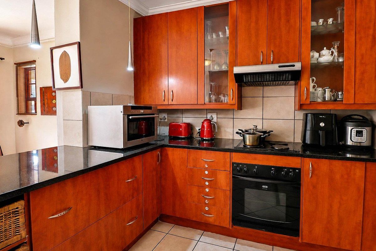 A functional kitchen featuring warm-toned wooden cabinetry, black granite countertops, built-in oven, electric cooktop, and tiled flooring with a neutral backsplash.