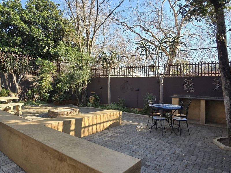 A private rear courtyard featuring paved flooring, a built-in braai area, and integrated masonry seating, surrounded by established trees and secure perimeter walls.
