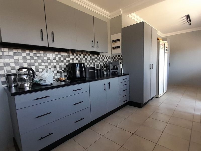 Modern kitchen featuring grey cabinetry, black countertops, and a distinctive checkered tile backsplash with tiled flooring.
