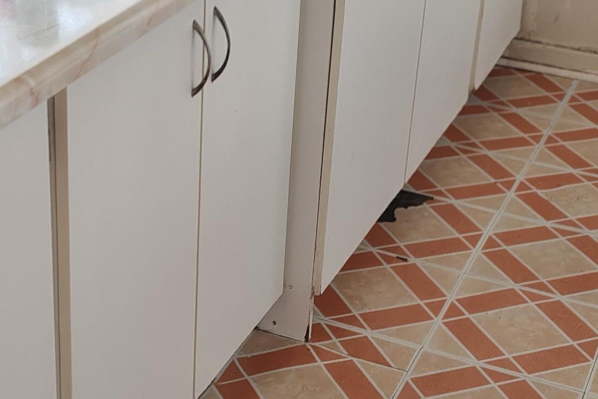 Close-up view of kitchen cabinetry featuring white doors, laminate countertops, and patterned ceramic floor tiles.