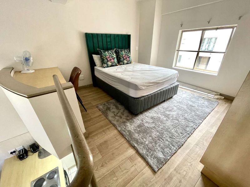 A bedroom featuring laminate flooring and a built-in counter area, with a staircase railing visible in the foreground.