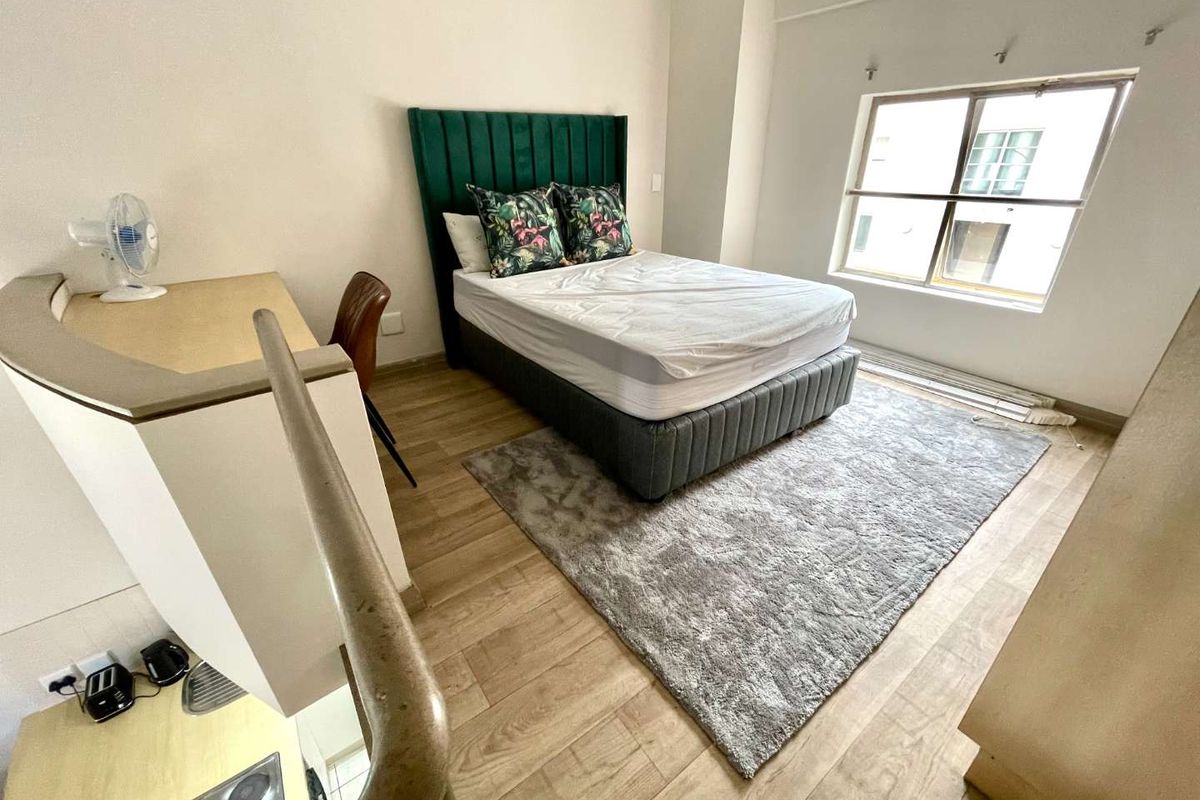A bedroom featuring laminate flooring and a built-in counter area, with a staircase railing visible in the foreground.