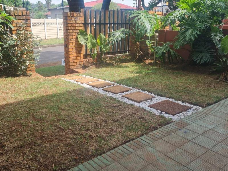 A well-maintained front garden featuring a brick boundary wall, metal fencing, and a decorative stone and paver walkway leading to the street entrance.