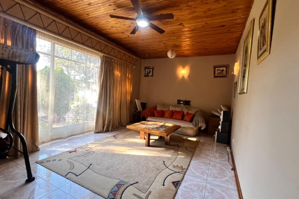 A spacious living room featuring a timber-clad ceiling, ceiling fan, and large sliding glass doors that provide ample natural light and garden access.