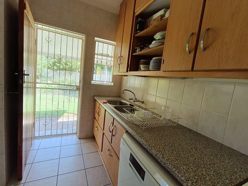 Functional scullery area featuring laminate cabinetry, granite countertops, double bowl sink, and direct access to the rear garden through a security gate.