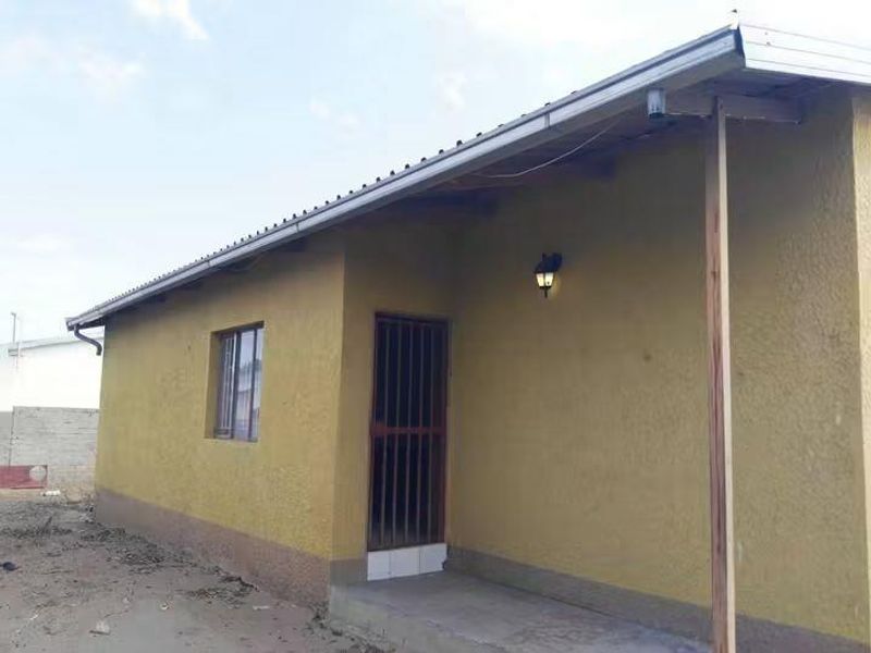 Rear exterior view of the house featuring a corrugated metal roof, security gate, and exterior wall lighting.