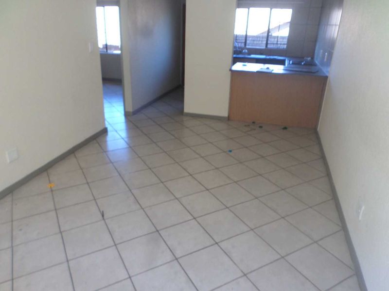 An open-plan living and kitchen area featuring neutral tiled flooring and a functional breakfast bar, presenting a blank canvas for interior design.