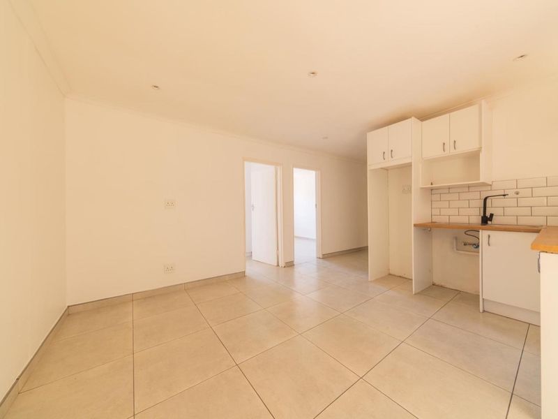 An open-plan living and kitchen area featuring neutral tiled flooring, white cabinetry, a subway tile backsplash, and recessed lighting.