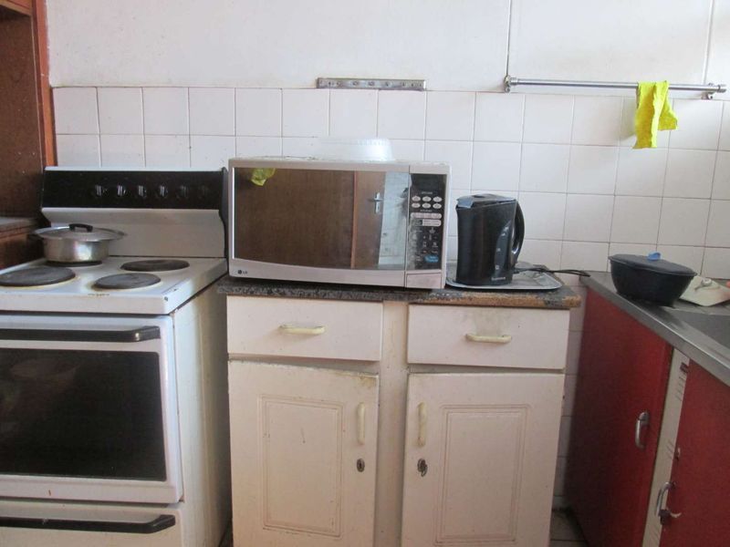 A dated kitchen area featuring a freestanding electric stove, tiled backsplash, and original cabinetry with stone countertops.