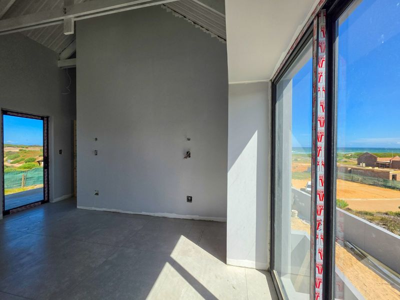 An empty, modern living area featuring vaulted ceilings, large sliding glass doors with ocean views, and neutral tiled flooring, currently in the final stages of completion.