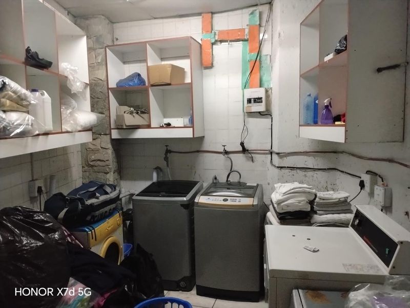 A functional laundry area featuring built-in cabinetry and tiled walls, currently showing significant signs of wear and exposed utility infrastructure.