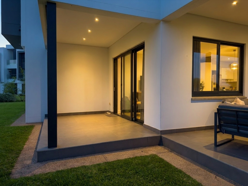 A modern covered patio featuring tiled flooring, recessed lighting, and sliding glass doors providing seamless access to the interior living space.