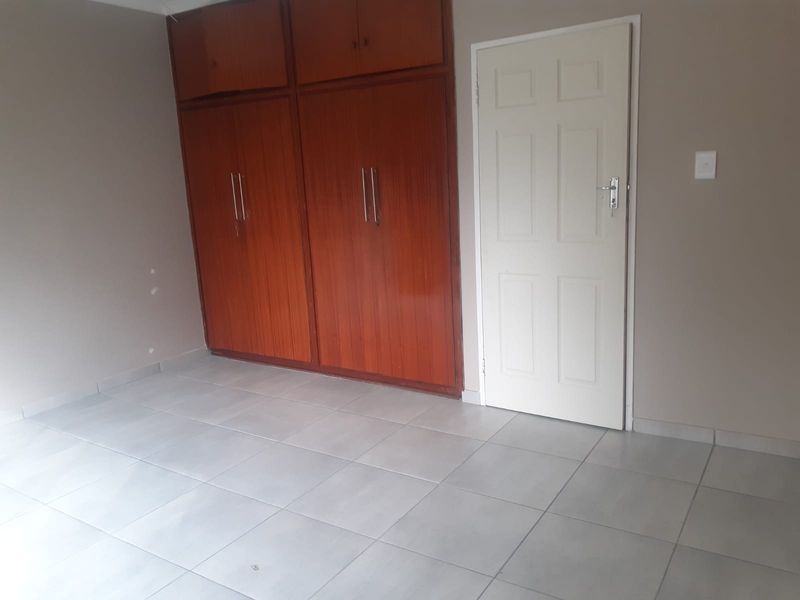 An empty bedroom featuring neutral tiled flooring and built-in wooden cupboards, providing a clean and versatile space ready for personalization.