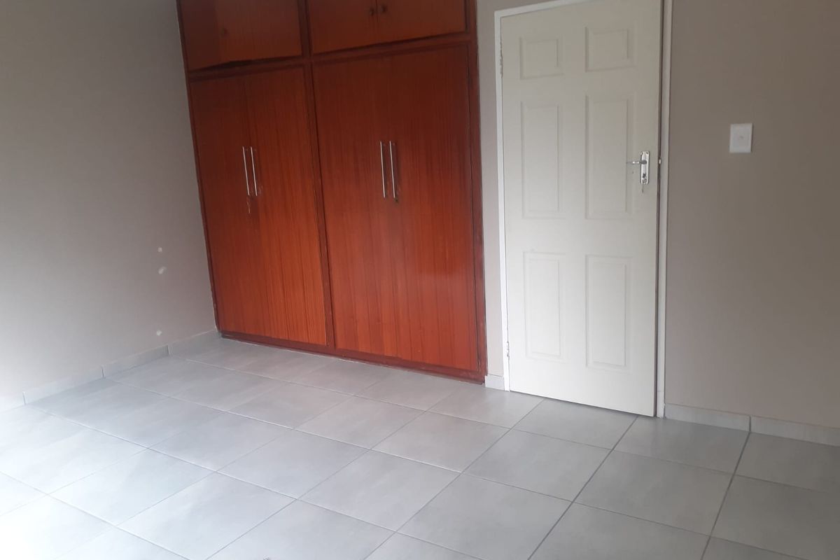 An empty bedroom featuring neutral tiled flooring and built-in wooden cupboards, providing a clean and versatile space ready for personalization.