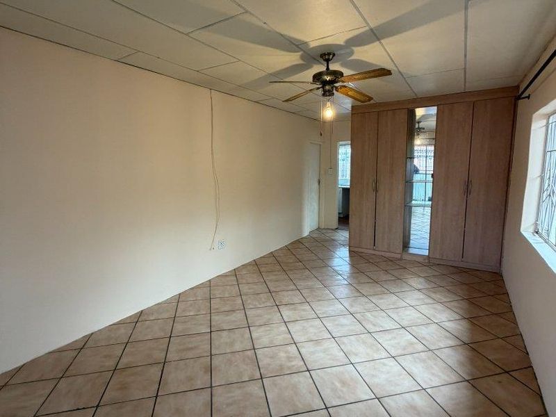 An empty bedroom featuring built-in cupboards, tiled flooring, and a ceiling fan, offering a blank canvas for renovation.