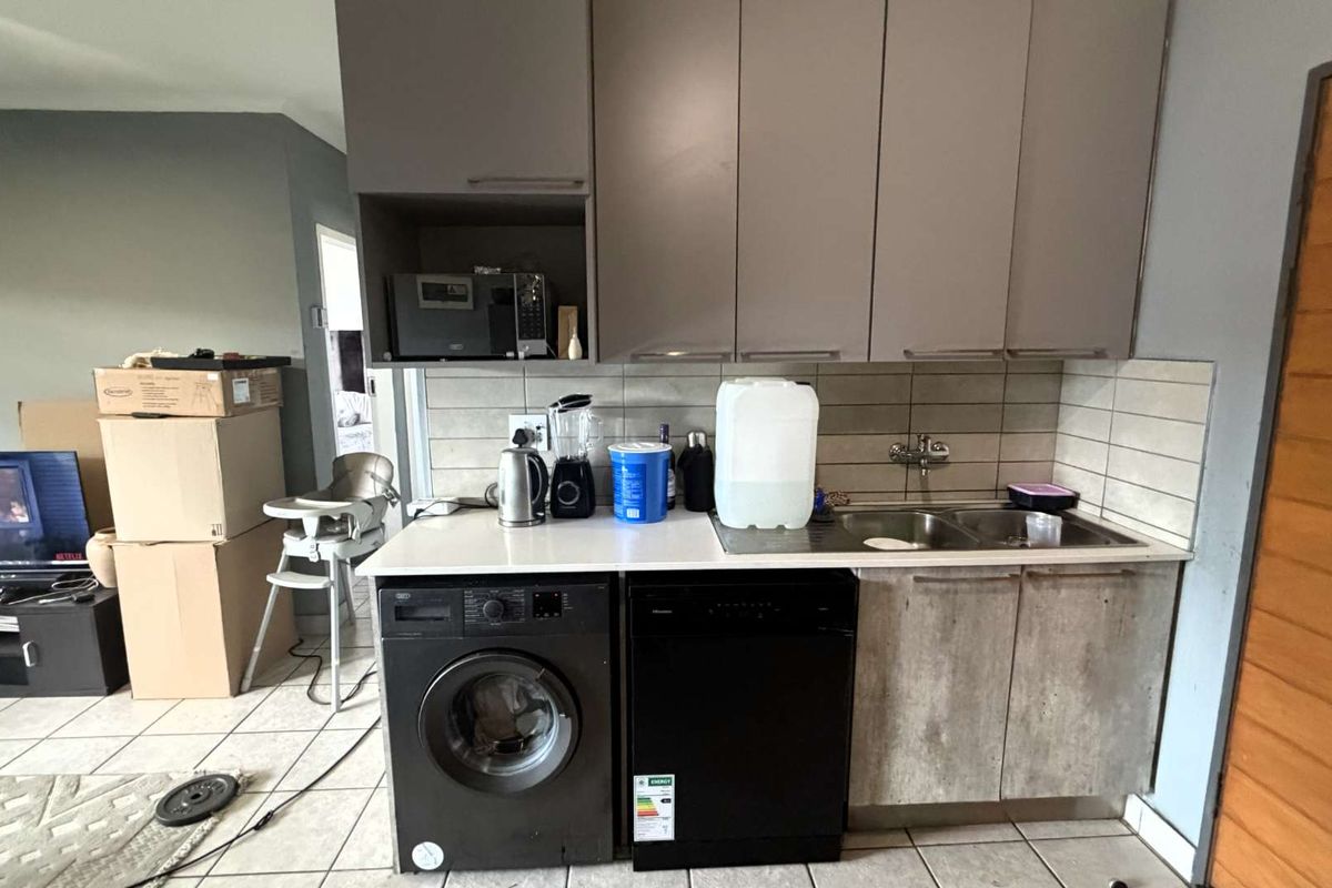 Compact kitchen area featuring built-in cabinetry, a double sink with mixer tap, tiled backsplash, and space for under-counter appliances.