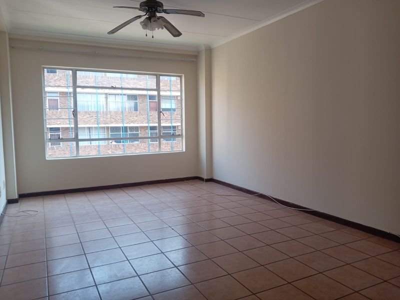A spacious, empty living area featuring neutral walls, tiled flooring, and a ceiling fan, offering a blank canvas for interior design.