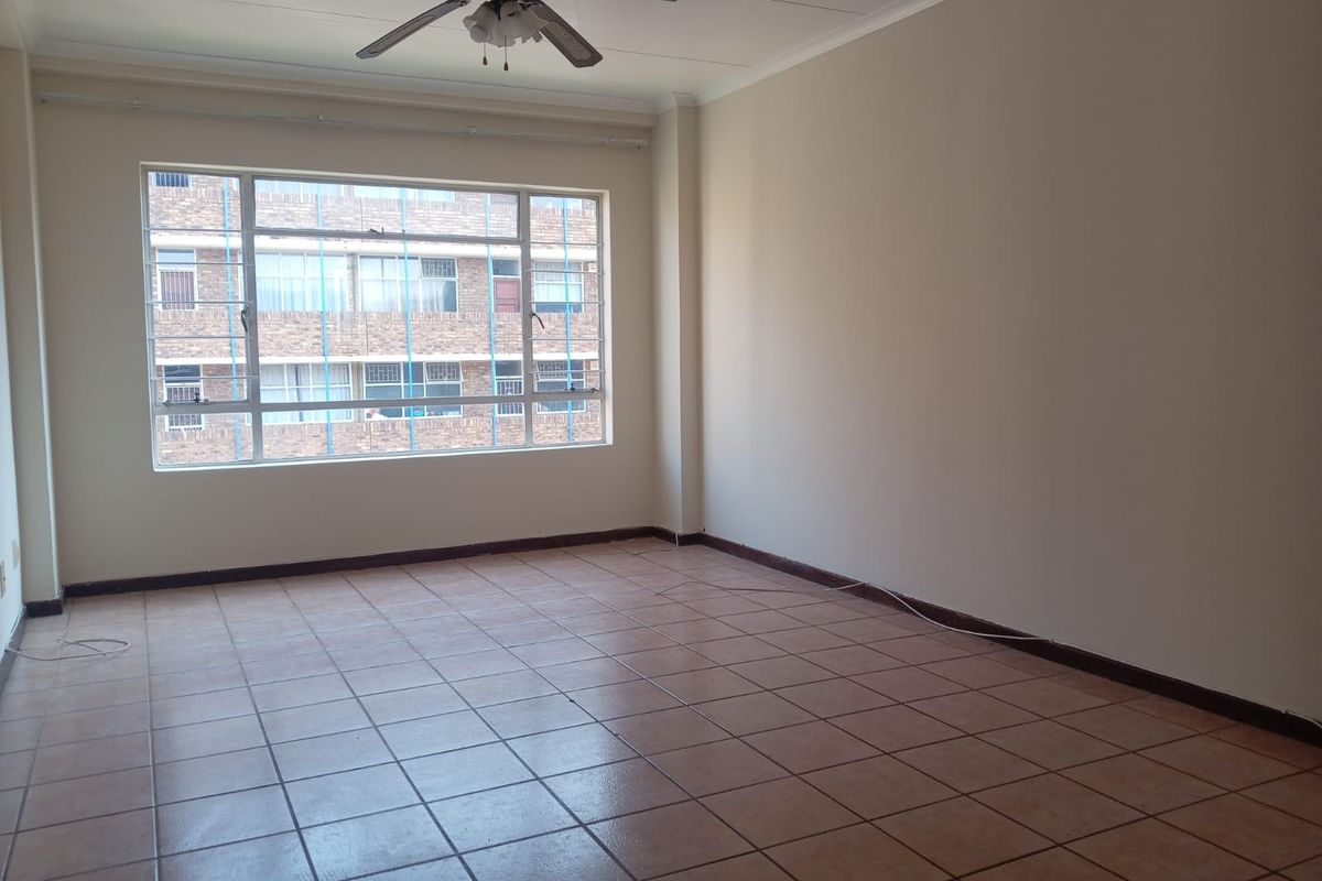 A spacious, empty living area featuring neutral walls, tiled flooring, and a ceiling fan, offering a blank canvas for interior design.