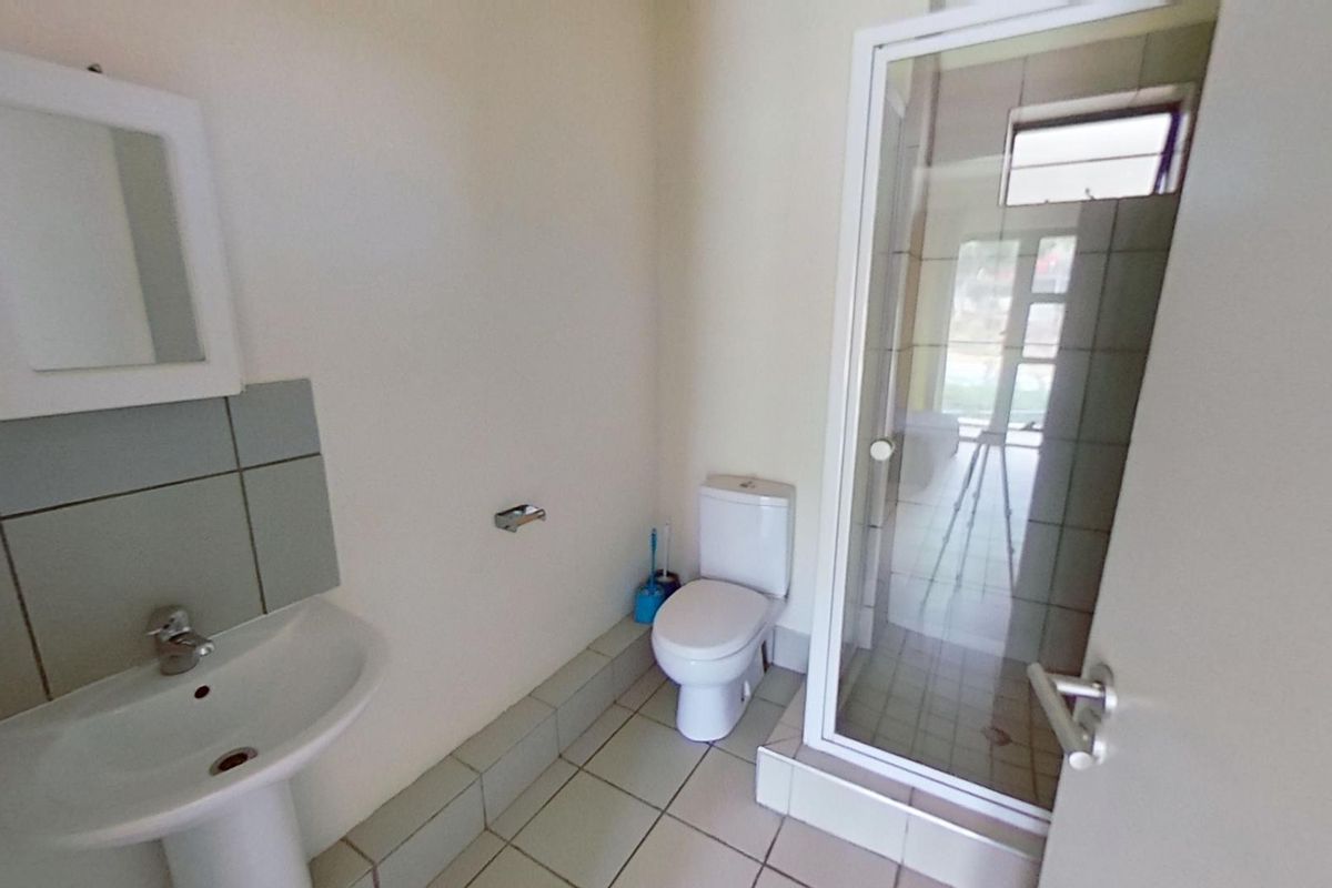 A functional bathroom featuring a pedestal sink, a toilet, and a glass-enclosed shower stall with tiled flooring.