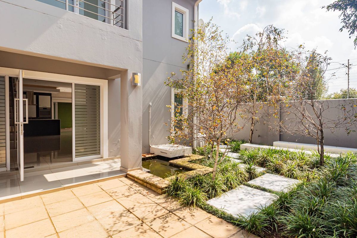 A private rear garden featuring a paved patio area, a small built-in water feature, and landscaped garden beds with stone stepping paths.