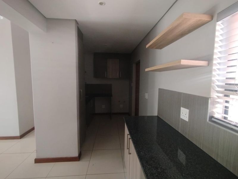 A modern, empty kitchen featuring granite countertops, built-in cabinetry, floating shelves, and neutral tiled flooring, offering a clean and functional workspace.