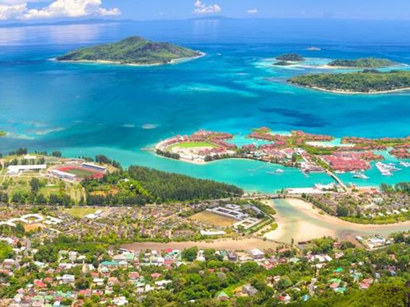 A panoramic aerial view showcasing the coastal landscape, surrounding islands, and turquoise waters of the Seychelles.