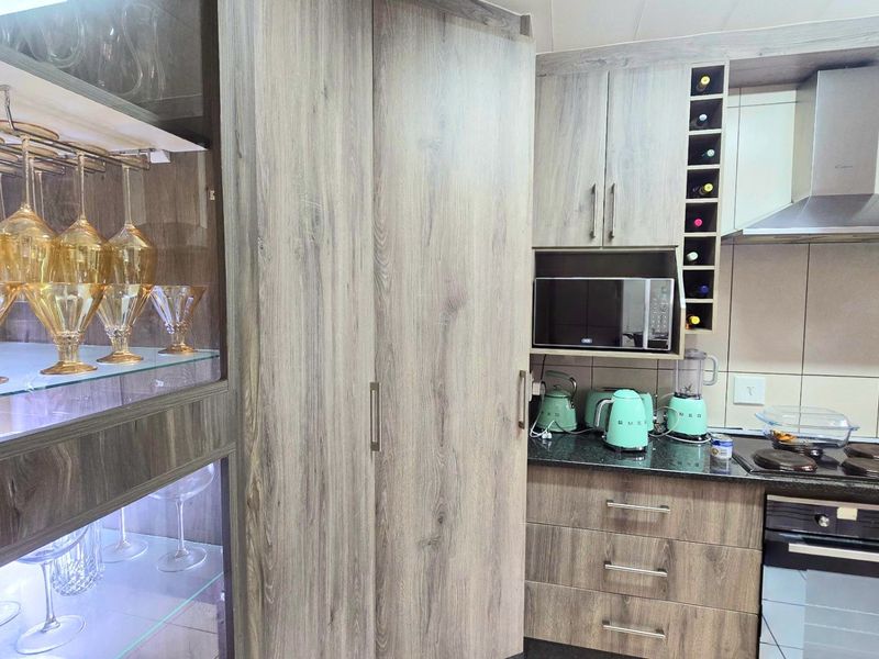Modern kitchen featuring wood-grain cabinetry, granite countertops, integrated appliances, and a dedicated glass-fronted display cabinet with internal lighting.