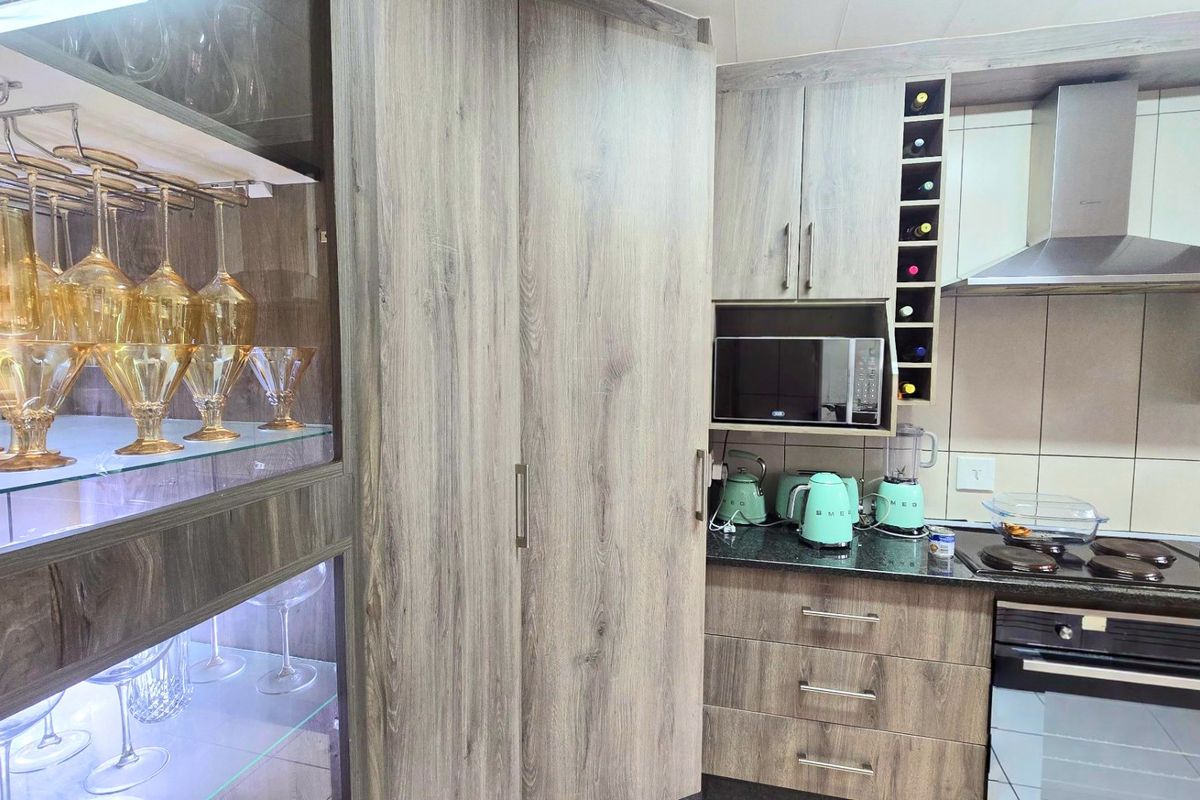 Modern kitchen featuring wood-grain cabinetry, granite countertops, integrated appliances, and a dedicated glass-fronted display cabinet with internal lighting.
