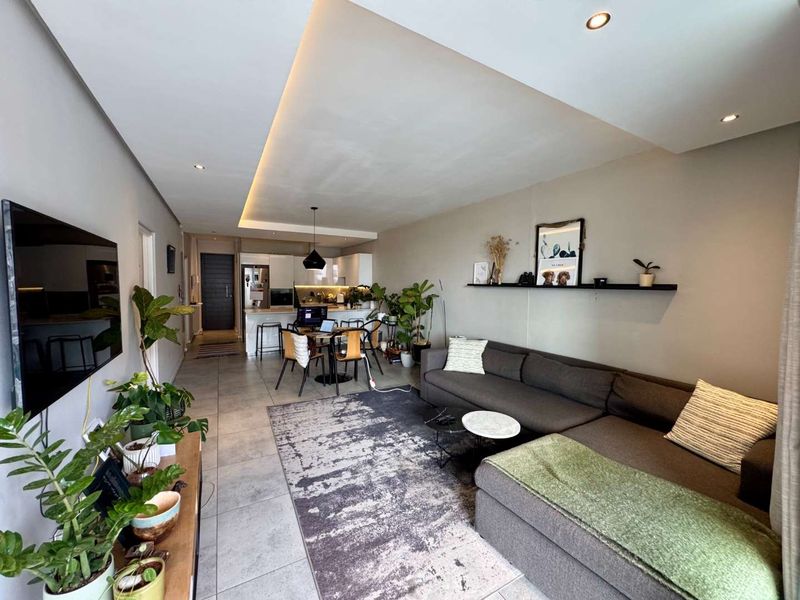 Modern open-plan living area featuring tiled floors, recessed cove lighting, and a sleek kitchen with built-in appliances and a central island.
